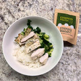 Bowl of food with chicken and cucumber salad with rice on a granite countertop next to a packet of Friendly Blends low FODMAP Essential Herbs seasoning.