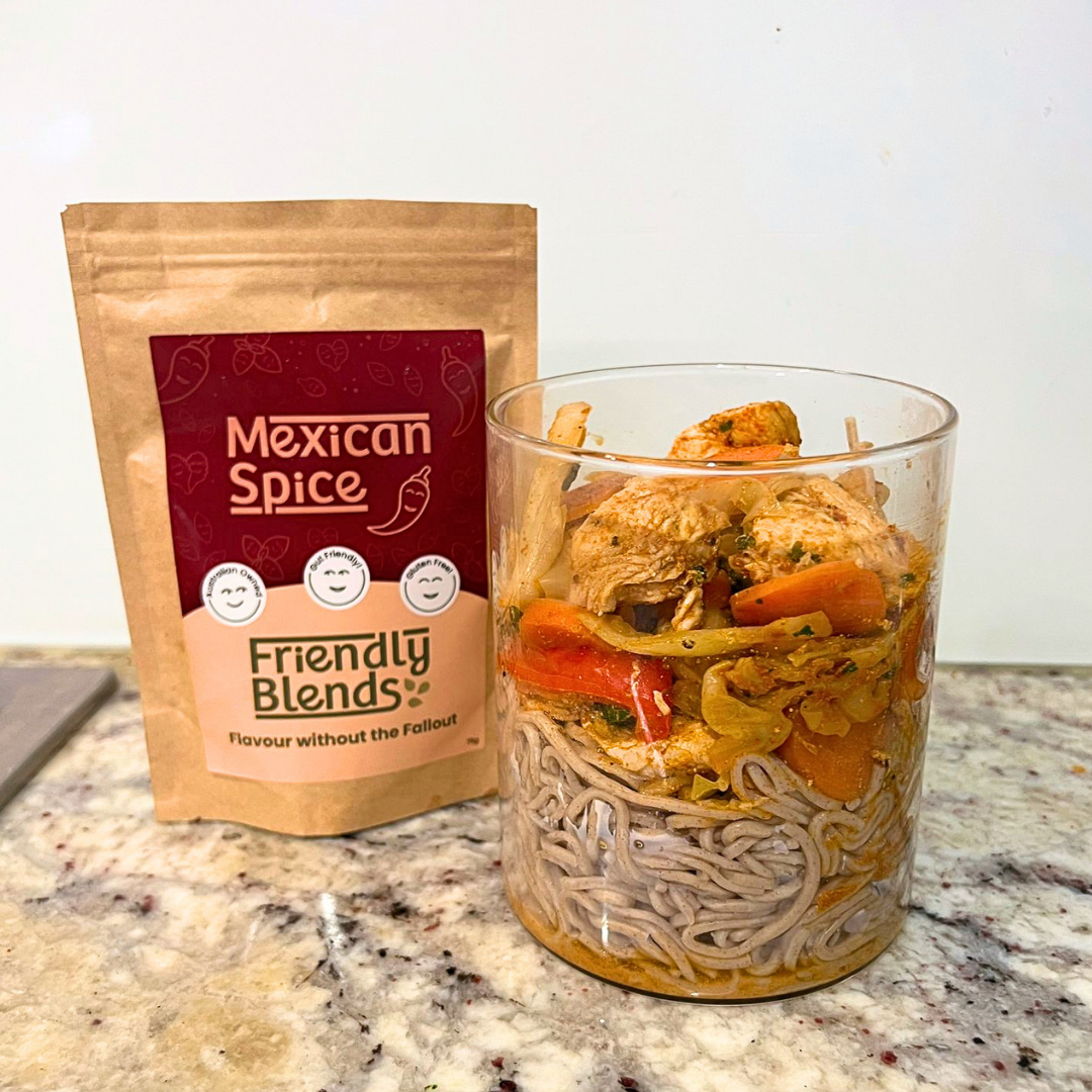 Soba Noodle Salad Bowl in a glass container beside a package of 'Friendly Blends low FODMAP Mexican Spice' on a countertop.